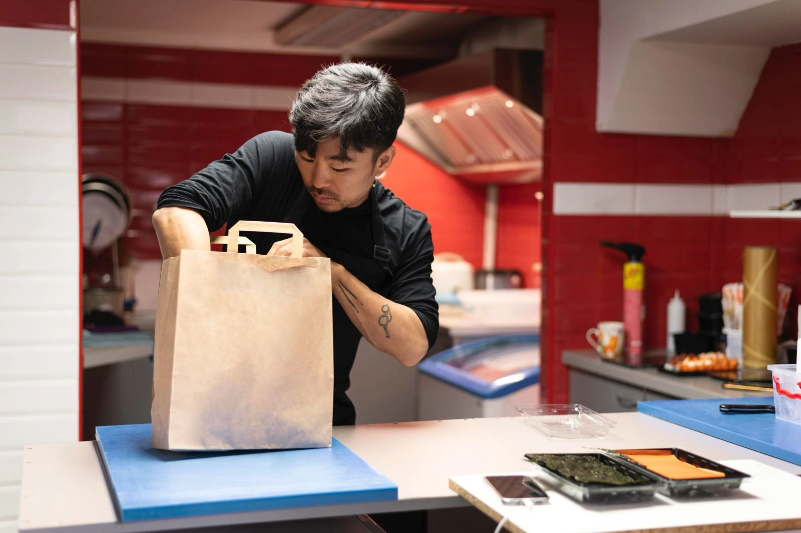 Seorang staf dapur memasukkan pesanan makanan ke dalam kantong kertas (paper bag) di dapur restoran