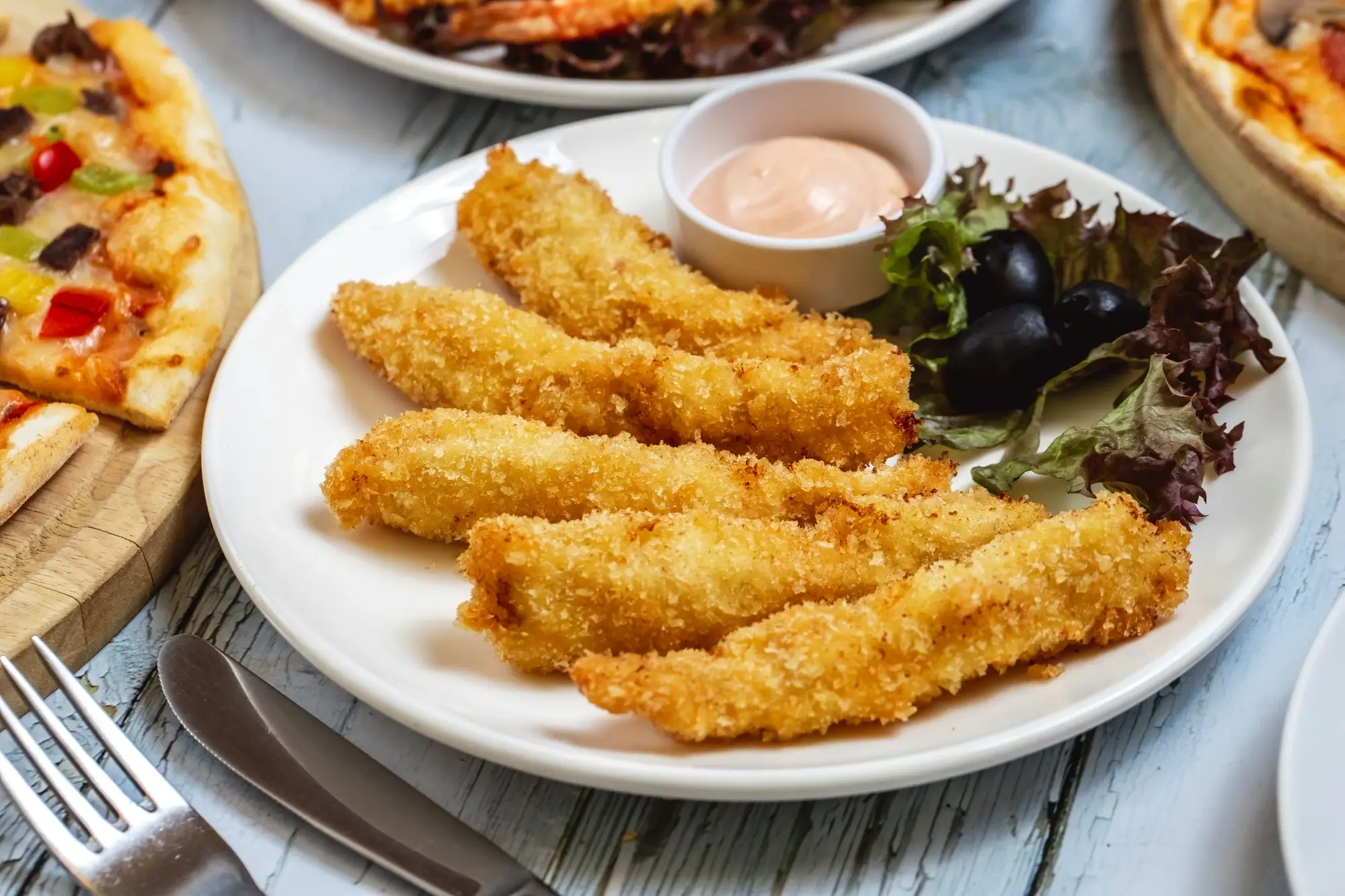 Chicken strips di atas piring dengan saus dan sayuran