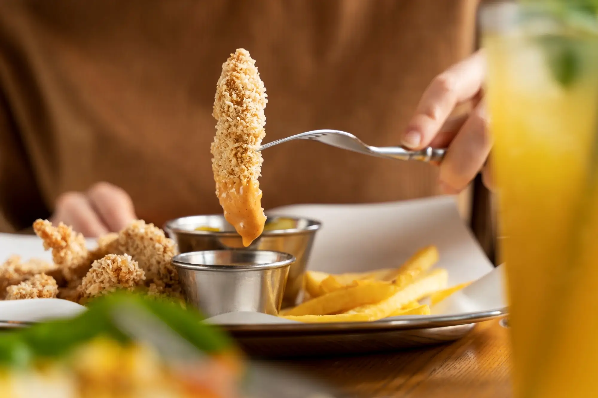 Seseorang memakan chicken strips yang telah dicelupkan saus keju